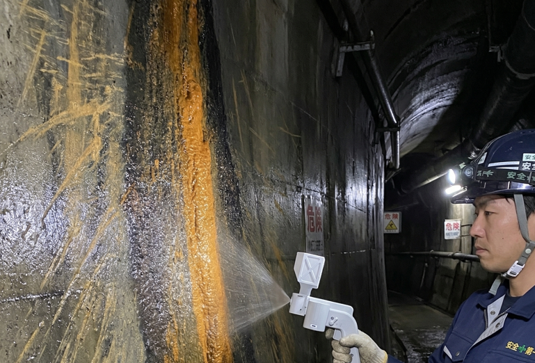 作業員がハンディスプレーでトンネル壁面の鉄バクテリア汚泥に除去剤を吹き付けている様子